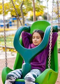 Low angle view of girl standing on swing at playground