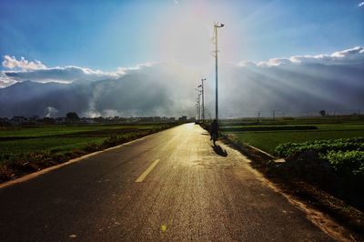 Empty road on grassy field against cloudy sky