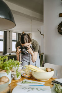 Young food stylist photographing through digital camera in studio