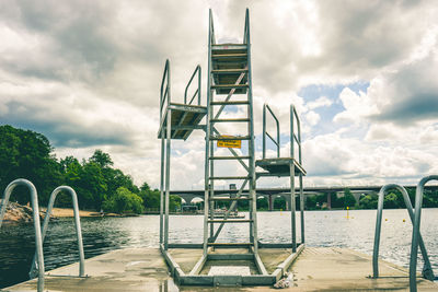 Ladder amidst lake against cloudy sky