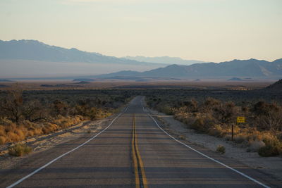 Empty road leading towards mountains against sky