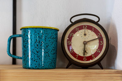 Close-up of antique clock and mug on table at home