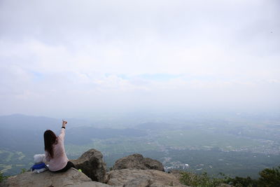 Rear view of man sitting on rock against sky