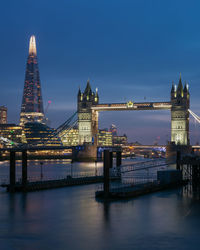 Illuminated tower bridge over river against sky in city 