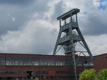 Low angle view of crane by building against sky