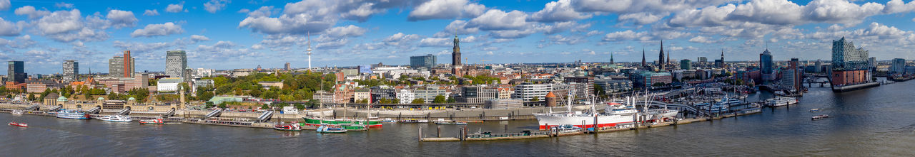 Panoramic view of sailboats in harbor by buildings against sky