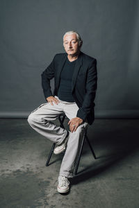 Mature man sitting on chair in front of gray backdrop