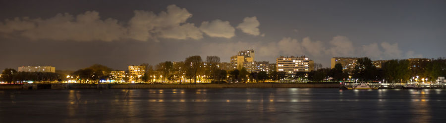 Illuminated city by sea against sky at night