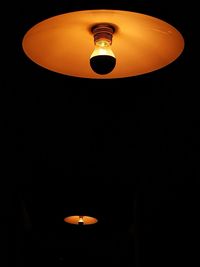 Low angle view of illuminated pendant light hanging against black background