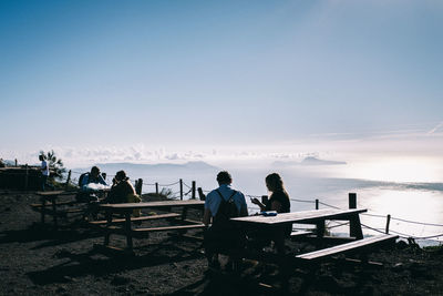 People sitting on bench looking at sea against sky