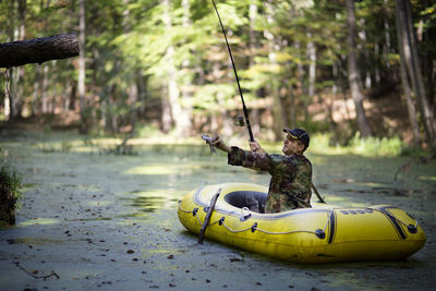 Man holding fish while sitting in inflatable raft on swamp