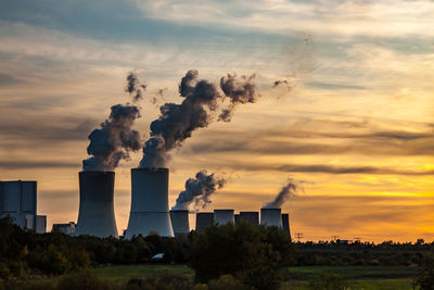 Smoke emitting from factory against sky during sunset