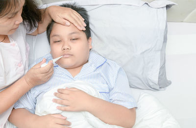 Woman checking ill son with thermometer at home