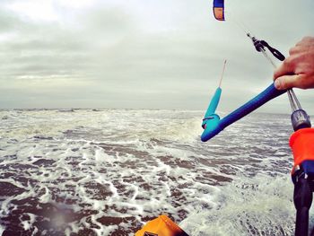 Cropped hand holding kite while kiteboarding in sea