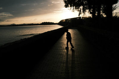 Silhouette man walking on footpath against sky during sunset