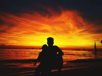 Silhouette couple sitting on beach at sunset