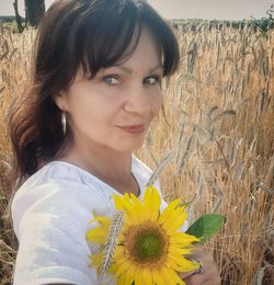 Portrait of smiling woman with yellow flower in field