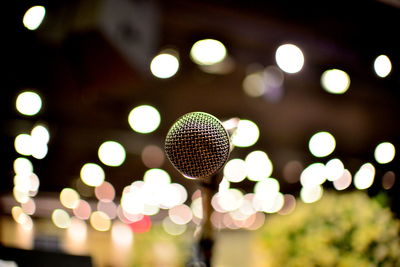 Close-up of microphone against illuminated lighting equipment at night