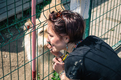 Side view of young woman looking through chainlink fence