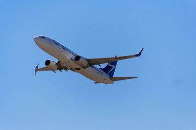 Low angle view of airplane flying against clear blue sky