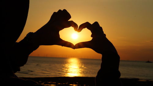 Silhouette man making heart shape against orange sunset sky