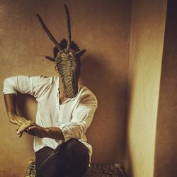 Man wearing wicker mask against wall