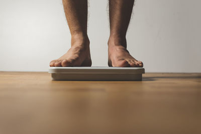 Low section of man standing on weight scale over hardwood floor at home