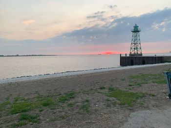 Lighthouse by sea against sky during sunset