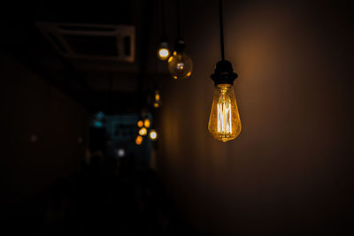 Low angle view of illuminated light hanging against wall in darkroom