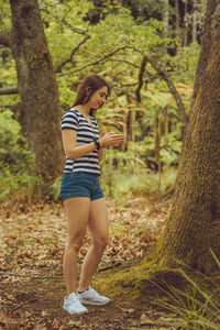 Full length of young woman looking at camera in forest