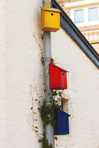 Multi-colored birdhouses on a drainpipe against the white wall of a building