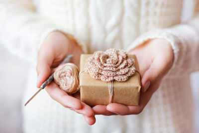 Woman holds present, coil of thread with crochet hook. gift with hand made crocheted flower. diy