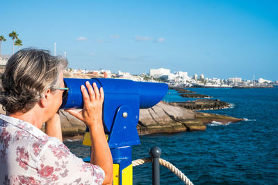 Woman looking through coin-operated binoculars at sea 