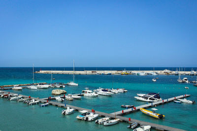 Sailboats moored in sea against clear blue sky