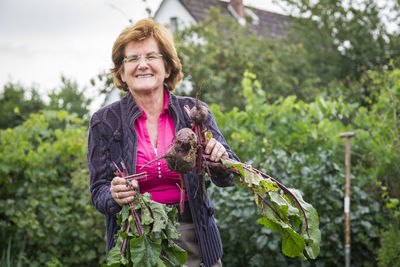 Portrait of smiling woman holding root vegetable against plants