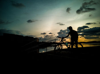 Silhouette man standing on railing against sky during sunset