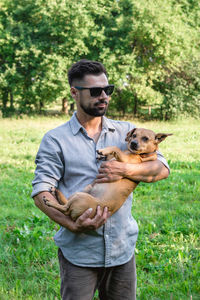 Handsome stylish european man is holding his dog in hands in park on a walk. 