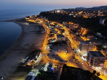 High angle view of illuminated city by sea against sky