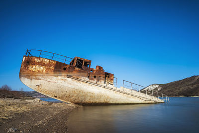 Abandoned ship by sea against clear blue sky