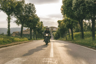 Couple riding motorcycle on road amidst trees against sky during sunset