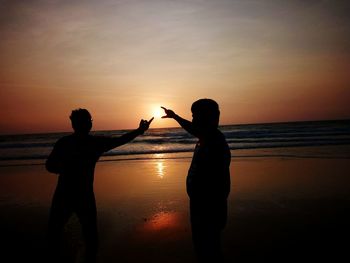 Silhouette men on beach against sky during sunset