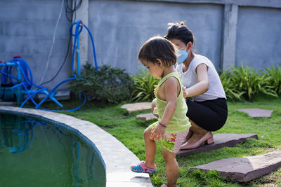 Mother and son watching koi fish at the pond in the garden behind the house. 