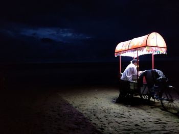 People sitting on beach by sea against sky at night