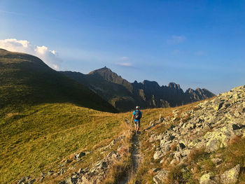 Rear view of man walking on field towards mountain against sky
