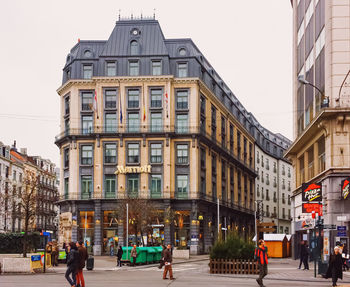 People walking on street amidst buildings in city against sky