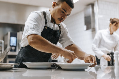 Focused male chef cleaning plate with napkin on kitchen counter at restaurant