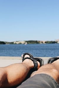 Low section of man relaxing at beach against sky