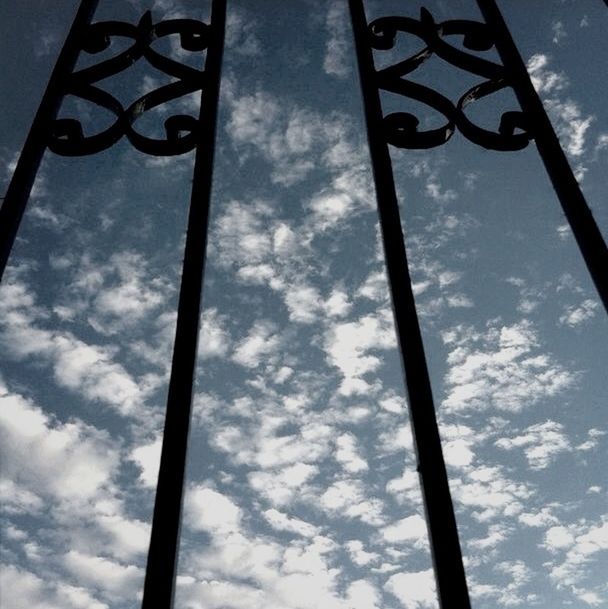 low angle view, sky, street light, cloud - sky, pole, lighting equipment, cloudy, cloud, metal, day, outdoors, no people, tree, sunlight, metallic, blue, hanging, nature, built structure, flag