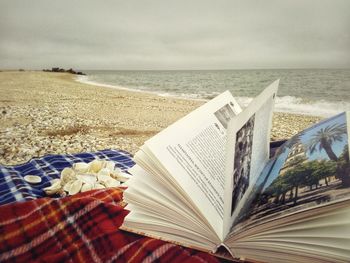 Close-up of book on beach against sky