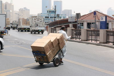 Man pulling boxes with push cart on road in city